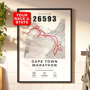 May include: Framed print featuring a red outline of the Cape Town Marathon route over a grayscale map. Includes race stats: "YOUR NAME" and "26593", date, distance (26.2 mi), and time. The text "YOUR RACE & STATS" is in a red speech bubble.