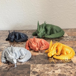 May include: Five sleeping dragon figurines in different colors: silver, black, orange, gold, and green. The dragons are all in a curled-up sleeping position.