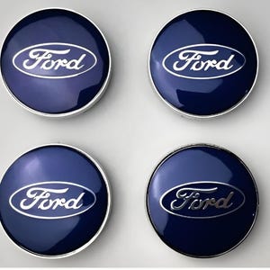 Puede incluir: Cuatro tapacubos Ford azul marino con el logotipo Ford plateado. Los tapacubos son redondos con una superficie brillante y reflectante. El logotipo de Ford está en cursiva.