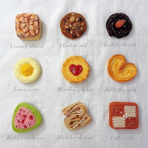 Könnte beinhalten: Neun gehäkelte Kekse in verschiedenen Formen und Farben. Die Auswahl umfasst Karamell-Mandel, Schoko-Nuss, Schoko-Mandel, Zitronencreme, Erdbeerkeks, Schmetterlings-Crisp, Matcha-Cranberry, Schwarztee-Kastanie und Kaffee-Keks. Jeder Keks hat ein einzigartiges Design.