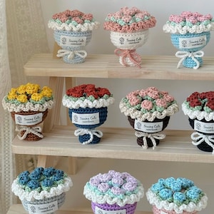 May include: A display of handmade crochet flower bouquets in a range of colours, such as pink, yellow, blue, and red. Each bouquet is presented in a small, decorative pot with a scalloped edge and a bow. The text "Sewing Cute Handmade" is visible on each bouquet.