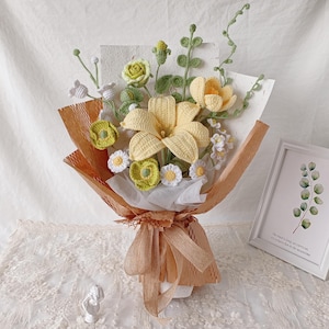 Pode incluir: Um buquê artesanal de flores de crochê em tons de amarelo, verde e branco. O buquê é embrulhado em papel pardo e amarrado com uma fita. O arranjo inclui grandes lírios amarelos, pequenas margaridas e outros detalhes florais.