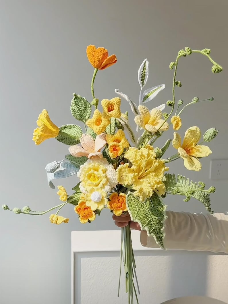 May include: A crocheted bouquet of yellow and orange flowers with green leaves. The flowers are arranged in a hand-tied bouquet.