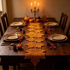 May include: A mustard yellow crocheted table runner featuring a repeating maple leaf pattern, centered on a dark wooden dining table set with ceramic plates, amber-colored glassware, gold-toned cutlery, small pumpkins, and pinecones.