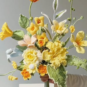 May include: A crocheted bouquet of yellow, orange, and white flowers with green leaves.