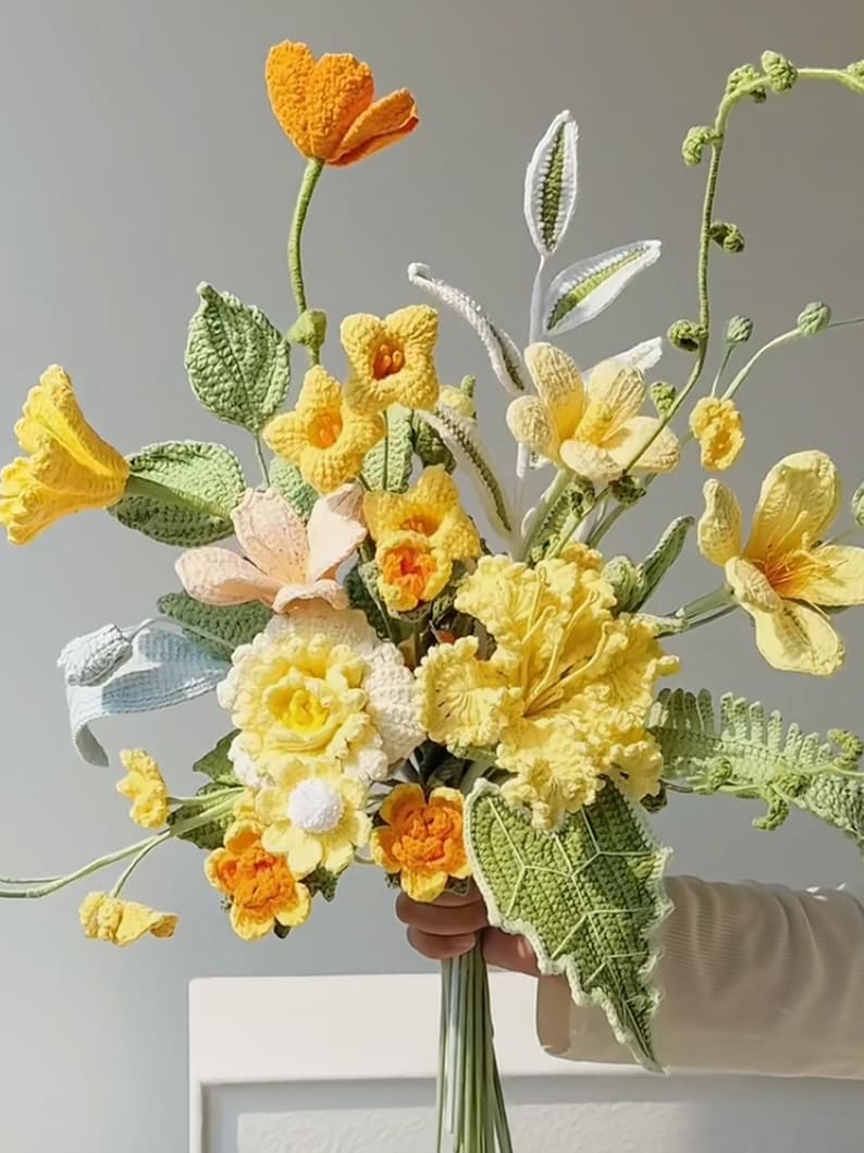 May include: A crocheted bouquet of yellow, orange, and white flowers with green leaves.