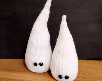 May include: Two handmade white knitted ghost figures with black button eyes. The ghosts have a teardrop shape and are standing on a wooden surface against a dark background. These whimsical decorations are perfect for Halloween or other spooky occasions.