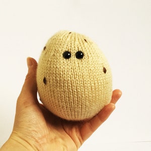 May include: A knitted beige potato toy with brown eyes and brown spots.