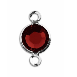May include: A silver-toned pendant with a round, red crystal. The pendant has two loops for attaching to a chain or cord.