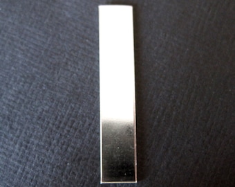 May include: A rectangular, metallic silver bar with a reflective surface. The bar is positioned vertically against a dark, textured background. The silver color transitions from bright at the top to a darker shade at the bottom.