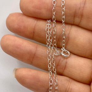 May include: A silver chain necklace with a lobster clasp closure. The chain is made of small, oval-shaped links.