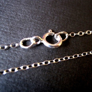 May include: Close-up of a silver chain necklace with a lobster clasp. The chain is made of small, oval-shaped links.