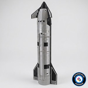 Può includere: Un modellino di razzo spaziale color argento e nero con punta conica, due alette laterali e un corpo cilindrico con linee di pannelli e dettagli strutturali visibili. Il razzo presenta un motivo nero testurizzato sulle alette e sulla punta.