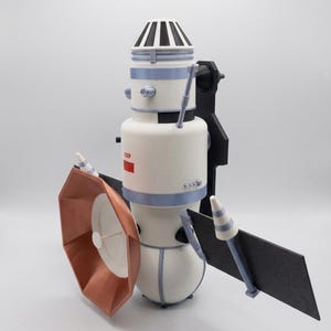 Könnte beinhalten: Ein 3D-gedrucktes Modell eines Weltraumsatelliten mit einem weißen zylindrischen Körper mit hellblauen Akzenten, einer großen kupferfarbenen achteckigen Schüssel, einem schwarzen rechteckigen Solarpanel und dem roten Text CCCP am Modul.