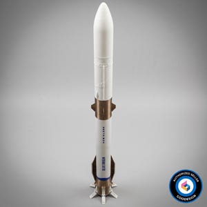 Op de afbeelding: Een verticaal model van de Blue Origin New Glenn raket met een wit cilindrisch lichaam, een puntige neuskegel, een metallic koperkleurig middengedeelte en vier landingspoten aan de basis. De tekst BLUE ORIGIN en NEW GLENN is zichtbaar.