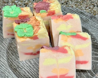 May include: Five handmade soap bars with floral designs. The soaps are layered with pink, yellow, and white swirls. Each bar has a different flower design on top, including a green flower, a pink flower, and a yellow flower.