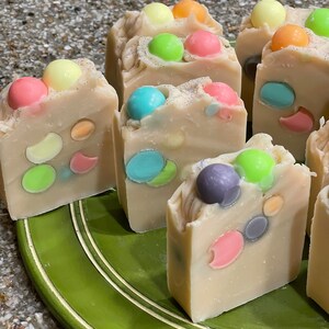 May include: A collection of handmade soap bars with colorful sprinkles embedded in the soap. The soap bars are arranged on a green plate.