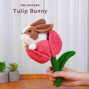 May include: A handmade crochet Tulip Bunny, featuring a bunny head with brown and white details emerging from a pink tulip. The green stem and leaves are visible. The text "PDF PATTERN Tulip Bunny" is at the top.