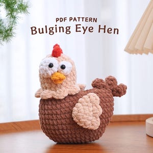 Könnte beinhalten: Eine gehäkelte braune und beige Henne mit großen weißen Augen und einem roten Kamm. Die Henne sitzt auf einer Holzoberfläche. Der Text "PDF PATTERN Bulging Eye Hen" wird über der Henne angezeigt.