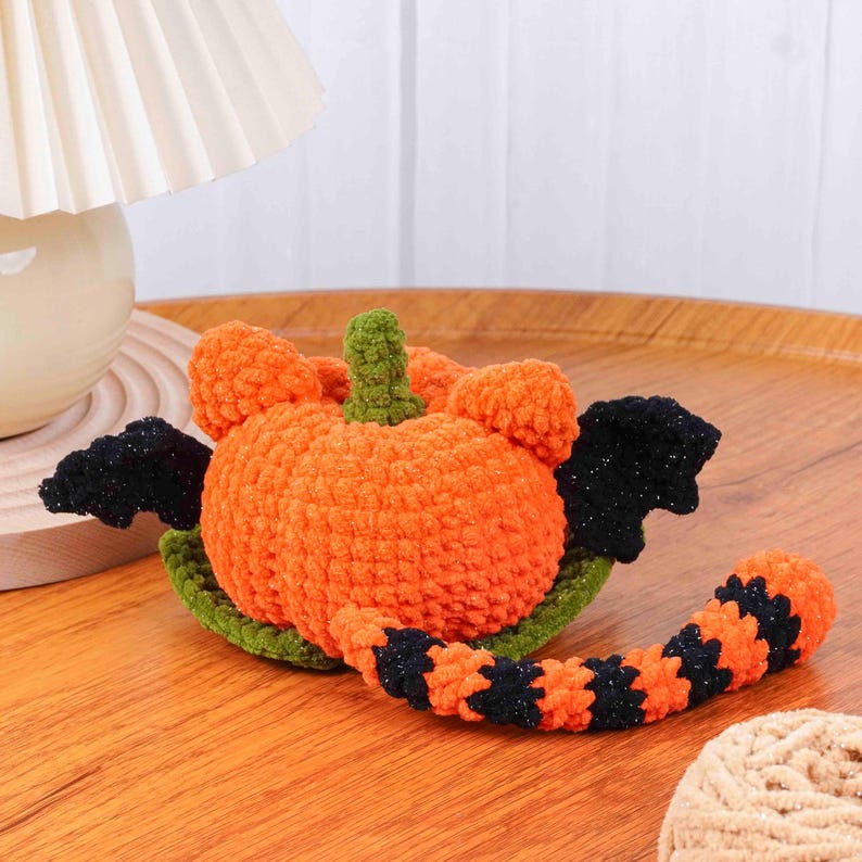 May include: A handmade, orange crochet pumpkin with green stem and base, and black wings and tail. The pumpkin is a Halloween decoration, perfect for fall. The tail is striped with black and orange.