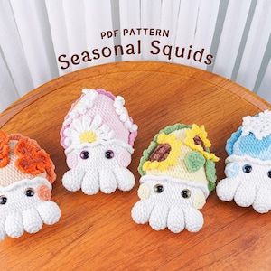 May include: Four handmade crochet squid toys with seasonal themes. The squid have white bodies and colourful hats, including orange leaves, a pink daisy, a yellow sunflower, and a blue snowflake. The text "PDF PATTERN Seasonal Squids" is at the top.