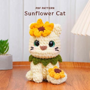 Pode incluir: Um gato de crochê com tema de girassol. O gato é creme com uma coroa de girassol amarela e uma gola verde. O texto "PDF PATTERN Sunflower Cat" está no topo. Um girassol menor está na base do gato.