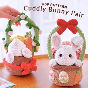 May include: Two crocheted bunny baskets with green yarn handles. One basket is filled with a white bunny and the other with a white bunny with pink ears. Both baskets have red bows.