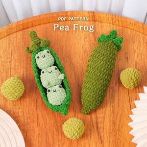 May include: A handmade crochet Pea Frog set, featuring a green pea pod with three frog figures, a single pea pod, and two round peas. The text "PDF PATTERN Pea Frog" is visible in the image. The items are on a wooden surface.