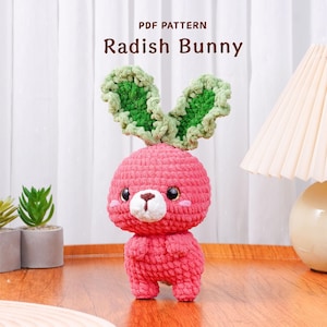 Può includere: Un coniglietto di ravanello all'uncinetto fatto a mano, rosa e verde. L'amigurumi presenta un corpo rotondo, braccia e gambe piccole e grandi orecchie verdi e frondose. Il testo "PDF PATTERN Radish Bunny" è visualizzato sopra il coniglietto.