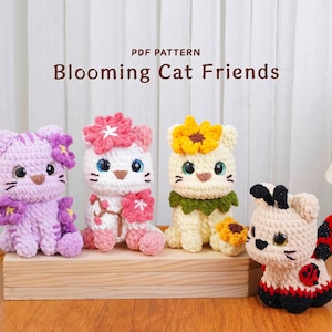 May include: Four crochet cat figures with floral accents and a ladybug-inspired design. The text "PDF PATTERN Blooming Cat Friends" is displayed above the figures. The cats are in shades of purple, white, and cream, with flower and sunflower details.