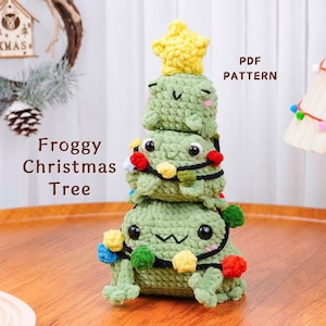 May include: A handmade crocheted Christmas tree in the shape of a frog, topped with a yellow star. The green tree is decorated with a string of colourful lights. The text "Froggy Christmas Tree" is visible. This is a PDF pattern.