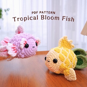 Könnte beinhalten: Zwei gehäkelte Plüschfischspielzeuge. Eines ist ein lila und rosa Fisch mit einer großen Flosse. Das andere ist ein gelber und grüner Fisch mit einer kleineren Flosse. Der Text "PDF PATTERN Tropical Bloom Fish" befindet sich über den Spielzeugen.