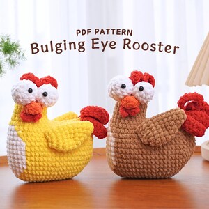 May include: Two crocheted rooster toys with bulging eyes. One rooster is yellow with a white chest and a red comb. The other rooster is brown with a white chest and a red comb. The toys are sitting on a wooden surface. PDF PATTERN Bulging Eye Rooster.