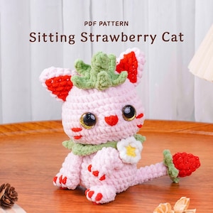 Peut inclure: Poupée chat fraise au crochet, assise. La poupée rose présente des détails rouges et verts, avec de grands yeux brillants. Le texte "PDF PATTERN Sitting Strawberry Cat" est visible au-dessus.