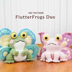 May include: Two crocheted frog figures with butterfly wings. One frog is green with blue and yellow wings, the other is pink with purple and yellow wings. The text "PDF PATTERN FlutterFrogs Duo" is above the frogs.