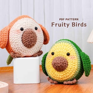 Op de afbeelding: Twee handgemaakte gehaakte vogelknuffels. Eén is oranje, crème en bruin, de andere is groen, geel en bruin, en lijkt op een avocado. De tekst "PDF PATTERN Fruity Birds" wordt boven de knuffels weergegeven. Deze zachte knuffels zijn perfect voor kinderkamers of als decoratie.