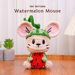 May include: A crocheted Watermelon Mouse plushie with a green watermelon hat and a red watermelon body. The mouse has pink ears and black eyes and whiskers. The text "PDF PATTERN Watermelon Mouse" is at the top of the image.