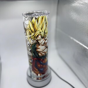 May include: A clear glass cylinder lamp with a colorful anime character design featuring a yellow-haired character with a red and orange outfit. The lamp has a white base.