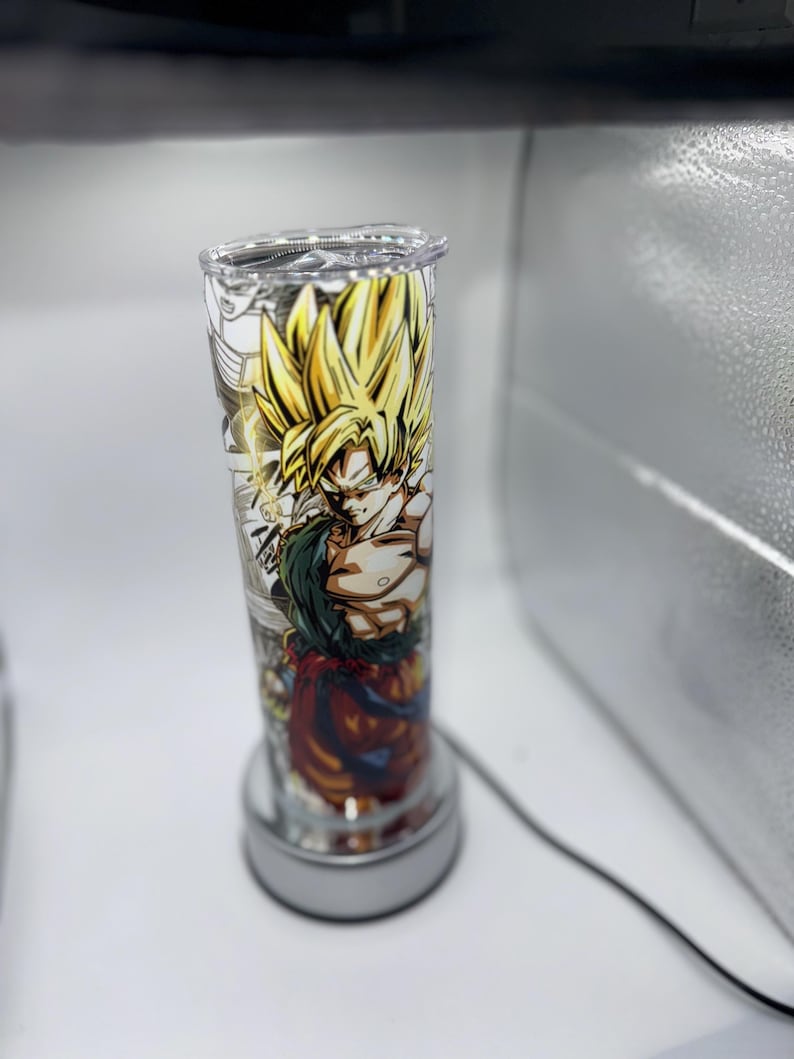May include: A clear glass cylinder lamp with a colorful anime character design featuring a yellow-haired character with a red and orange outfit. The lamp has a white base.
