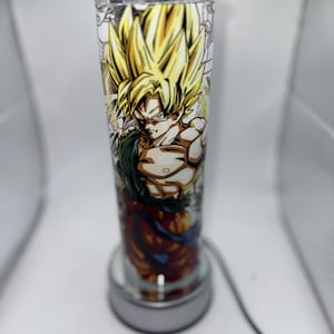 May include: A clear glass lamp with a white base and a colorful image of a cartoon character with spiky yellow hair. The character is wearing a red and orange outfit and has a determined expression.