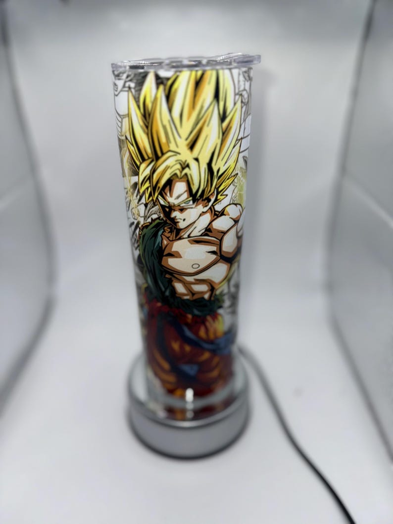 May include: A clear glass lamp with a white base and a colorful image of a cartoon character with spiky yellow hair. The character is wearing a red and orange outfit and has a determined expression.