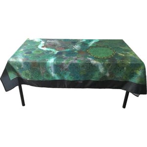 May include: A rectangular tablecloth featuring a green and blue landscape design. The tablecloth is draped over a table with black legs. The edges of the tablecloth have a black border.
