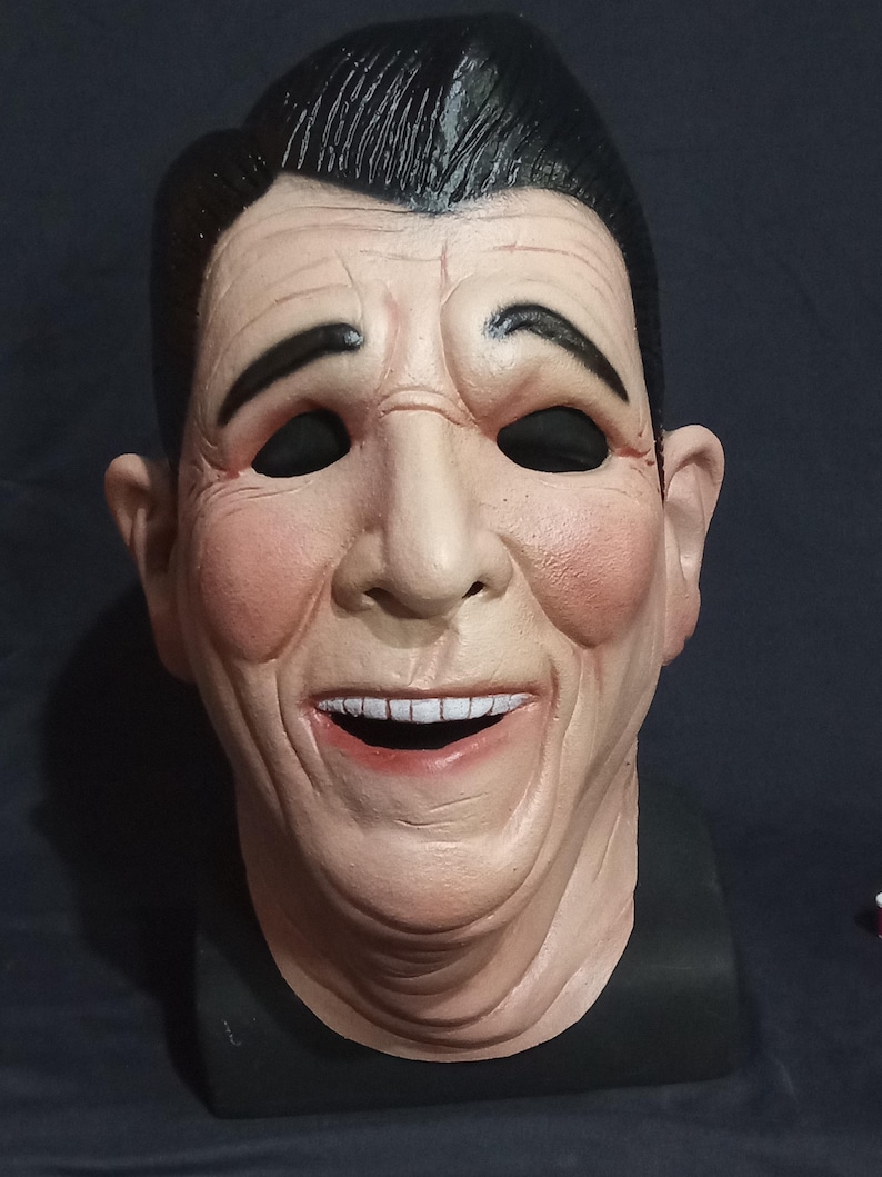 May include: A realistic-looking mask of a man with a wide smile, black hair, and black eyes. The mask is made of a light-colored material and has a textured surface.