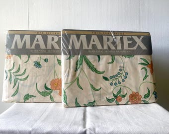 Puede incluir: Dos paquetes de sábanas Martex para cama individual, una bajera y una encimera, con tela de color crema y un estampado floral de enredaderas verdes, flores naranjas y bayas azules. El embalaje incluye la marca Martex en letras negritas.