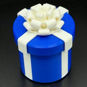 May include: A blue cylindrical gift box with white ribbon and a large bow on top. The box has vertical white stripes. The bow and ribbon are white. The gift box is a perfect present for any occasion.