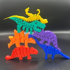 May include: A stack of five colorful articulated dinosaur toys. The dinosaurs are made of plastic and are in the colors yellow, green, orange, purple, and blue.