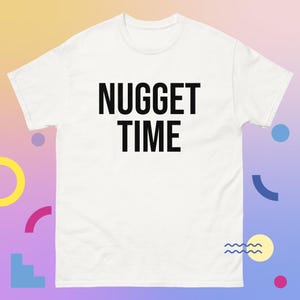 Puede incluir: Camiseta blanca con la frase "NUGGET TIME" impresa en letras negras grandes. La camiseta tiene cuello redondo y mangas cortas. La tela parece suave y cómoda.