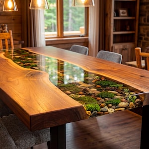 May include: A large, rectangular wooden dining table with a clear resin river running through the center. The river is filled with stones, moss, and small plants. The table is surrounded by chairs and a bench.
