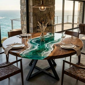 May include: A circular wooden dining table featuring a turquoise resin river design. The table is set with plates, cutlery, and napkins. The room has large windows overlooking the sea, with six wooden chairs around the table.