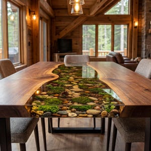 May include: A large, rectangular wooden dining table with a river of resin filled with stones and greenery. The table is surrounded by upholstered chairs in a rustic, cabin-style interior. The table is approximately 10 feet long.